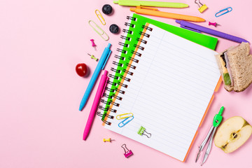 School background with notebooks, sandwich for lunch and colorful study supplies over pink. Back to school concept with copy space for text.