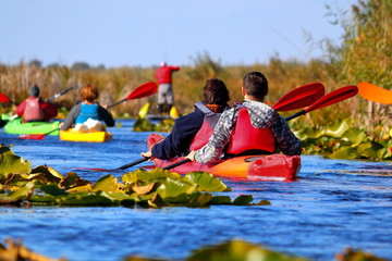 Kayakers row on the river among water lilies on a sunny autumn day