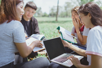 Group of student used computer and reading books on lawn. education and technology concept.