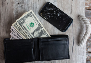 Crashed black smartphone and money in leather wallet to buy a new one. Dollars and broken phone on the woodeh background. Time to get a loan for electronics.