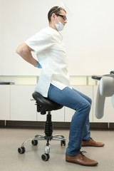 Dentist with lower back pain stretching at work in his office 