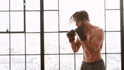 Athletic man punching a heave punching bag in a loft style gym.