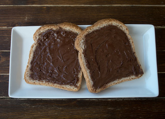 Slices of bread with hazelnut cream on a wooden table seen from above