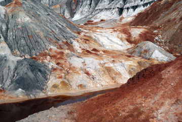 landscape of a multi-colored weathered hilly desert with a poisonous river with red water