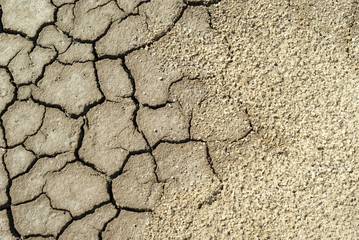 Fototapeta premium background - cracked dry sun-dried clay crust in a waterless desert half sanded with sand