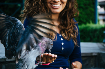 A smiling woman feeding a pigeon from her hand