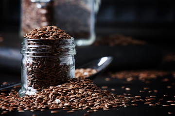 Flax seeds in glass jar, brown background, selective focus