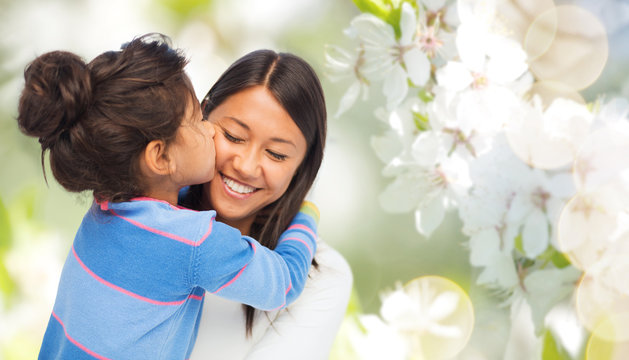 family, motherhood and people concept - happy mother and daughter hugging and kissing over cherry blossom background