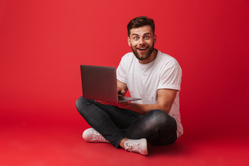 Happy young man sitting isolated using laptop computer.
