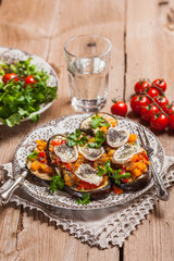 Baked eggplant with yellow and red bell pepper, tomatoes, garlic, goat cheese and chia seeds in plate on an old wooden rustic table