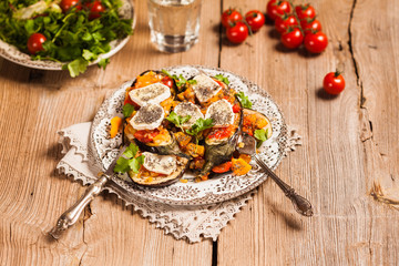 Baked eggplant with yellow and red bell pepper, tomatoes, garlic, goat cheese and chia seeds in plate on an old wooden rustic table