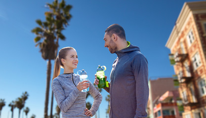 fitness, sport and people concept - smiling couple with bottles of water over venice beach background in california