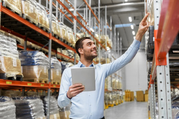 logistic business, technology and shipment concept - happy businessman with tablet pc computer checking goods at warehouse