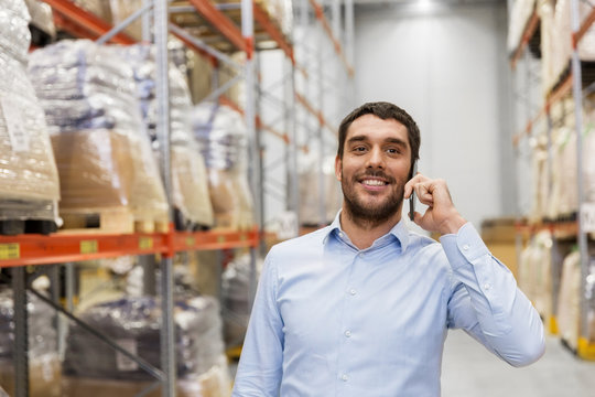 wholesale, logistic business and people concept - smiling businessman calling on smartphone at warehouse