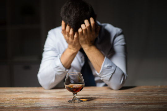 alcoholism, alcohol addiction and people concept - male alcoholic drinking brandy on table at night