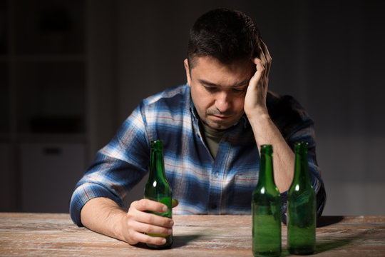 alcoholism, alcohol addiction and people concept - male alcoholic with bottles drinking beer at table at night