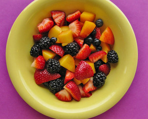 Fresh, colorful summer fruit salad in green bowl on red-violet background
