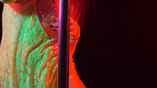 Sexy woman in rhinestones lace costume with shining stones. Striptease dancer moving hips on stage in night club with pylone. Stripper entertains visitors. Slow motion.