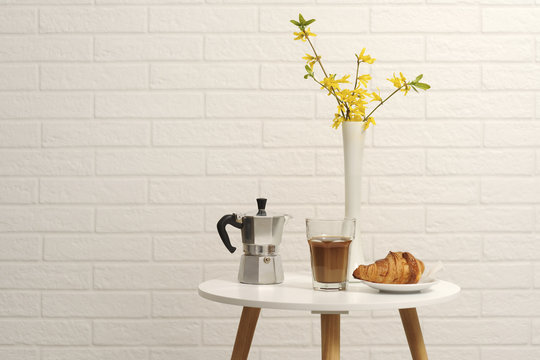 Close-up of croissant with coffee and espresso maker by flower vase on table by wall