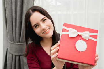 Happy pretty young woman holding gift box in the house