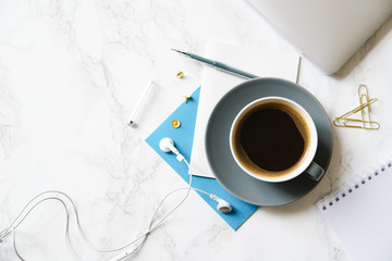 Workplace flatlay with laptop, blue card and coffee cup on marble table