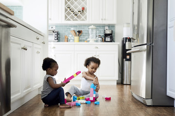 Sisters playing with toy blocks while sitting on hardwood floor in kitchen at home