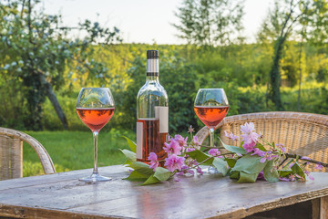 French art of living/Bottle of pink wine and two wineglasses on old wooden table outdoors