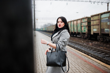 Brunette girl in gray coat posed in railway station.
