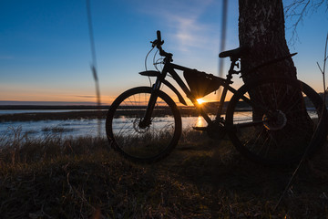 Fototapeta na wymiar Silhouette of a bicycle standing near a tree against the backdrop of the setting sun