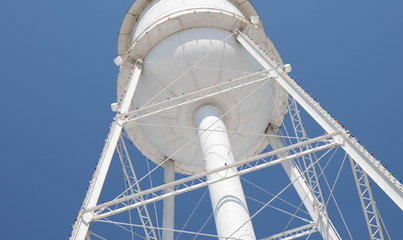 Looking up at a bright white water tower from below with a bright blue cloudless sky.