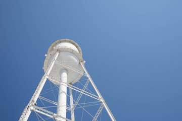 Looking up at a bright white water tower from below with a bright blue cloudless sky. - Powered by Adobe