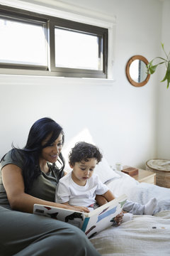 Mother and son looking at picture book while relaxing on bed at home