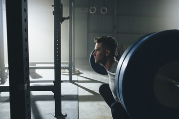 Side view of confident male athlete lifting barbell at gym