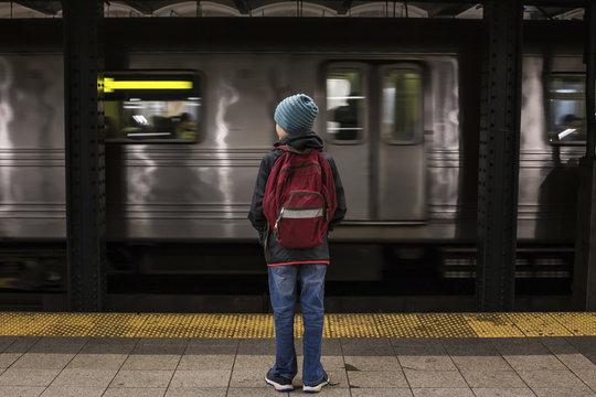 Rear view of boy with backpack standing at subway station