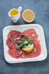 Carpaccio beef served on a white plate with fresh arugula, parmesan cheese, lemon and olive oil, vertical shot