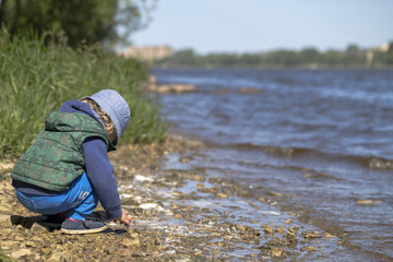 A young boy play close to river under blue sky