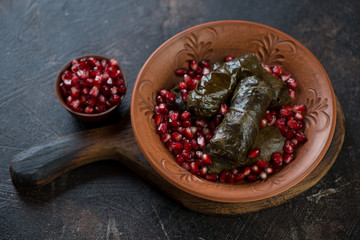 Clay plate with dolma or dolmades and pomegranate seeds on a dark brown stone background, studio shot