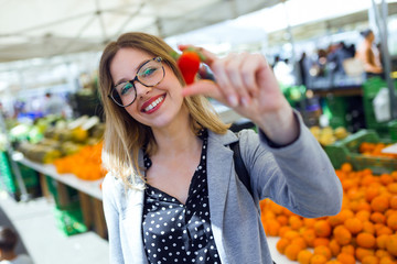 Pretty young woman showing strawberry to camera in the street market.