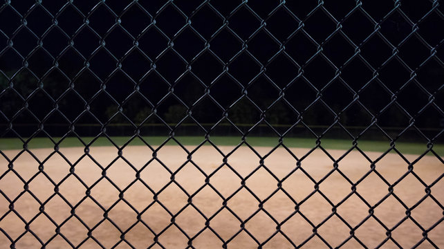 Close up photo of a baseball field fence looking through it to an empty field at night.  Great for background use.