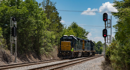 A long view of two railroad cars with flashing signals and an engineer standing on the back.  (high...