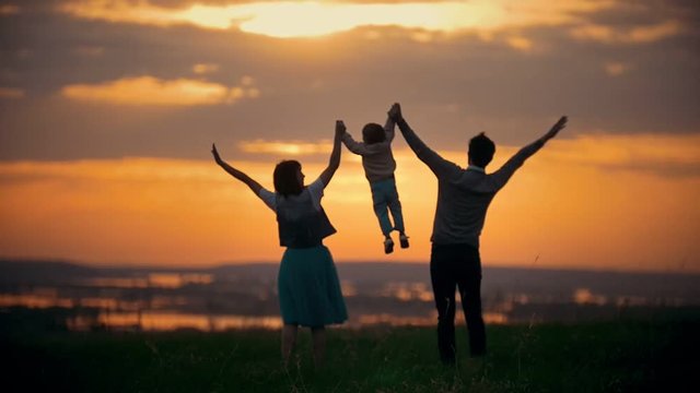 Family holding hands dad and mom raise the baby in the air, the family has fun, orange sunset, summer