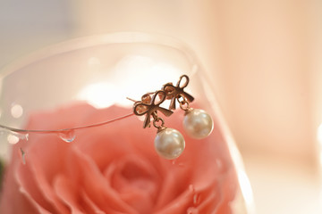 pearl earrings with golden bows hang on a glass with a pink rose