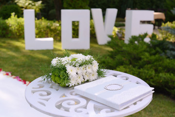 wedding guest book and box for money and gifts decorated with fresh flowers against the background of three-dimensional white letters LOVE in the defocus