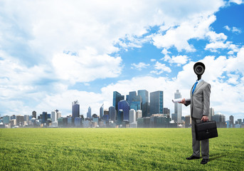 Camera headed man standing on green grass against modern cityscape