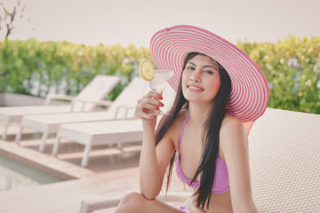 Swimsuit Concept. Beautiful girls in swimwear are drinking. Asian girls drink fruit juice at the pool. Beautiful girl in swimwear is happy at the pool.