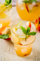 Peach and lime lemonade, mojito cocktail with fresh fruit garnish, om light concrete background copy space selective focus