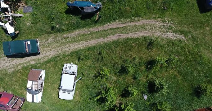 Aerial view of broken rusty cars amidst greenery, the field lined with old machines for disassemble