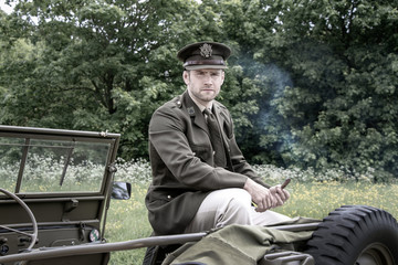 Handsome American WWII GI Army officer in uniform smoking cigar while sitting on Willy Jeep