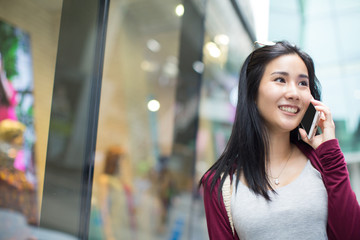 Asia woman walking and talking with a smart phone in the street in a sunny summer day