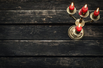 Old candlestick with four burning candles on an empty wooden table background with copy space.